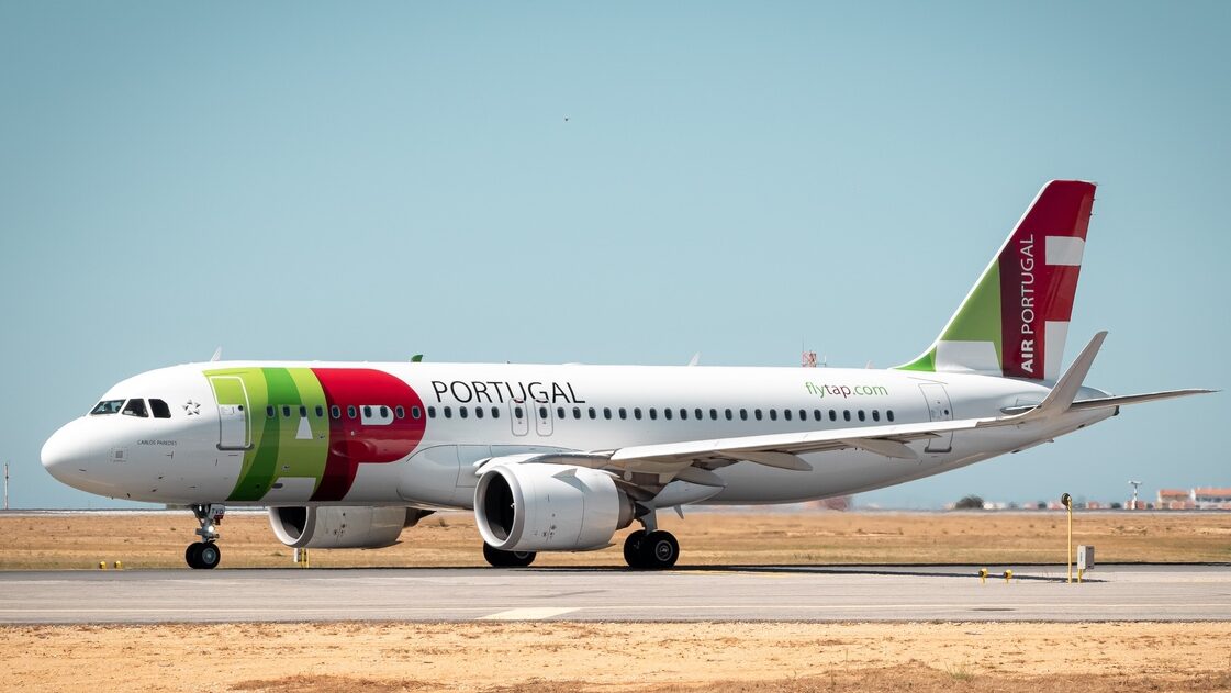 Avião da TAP Air Portugal estacionado numa pista de aeroporto, com céu limpo ao fundo, ilustrando operações aéreas na Madeira.