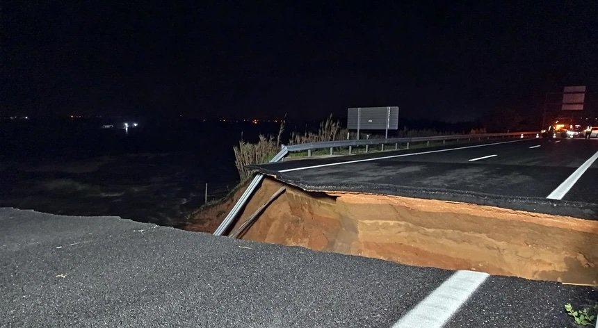 Estrada cortada abruptamente devido ao desabamento de parte do viaduto, com uma grande secção do asfalto desaparecida e o interior exposto, durante a noite, ilustrando os danos causados pelas cheias na zona de Coimbra.