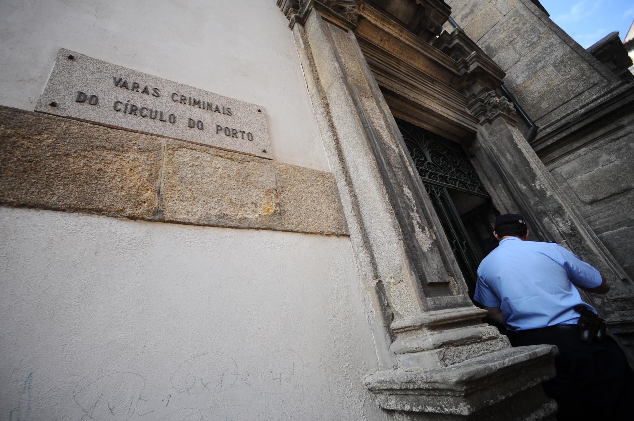 Entrada do Tribunal de São João Novo, com fachada em pedra e um agente policial junto à porta, ilustrando o ambiente institucional referido no artigo sobre dificuldades logísticas e de recursos humanos no tribunal.