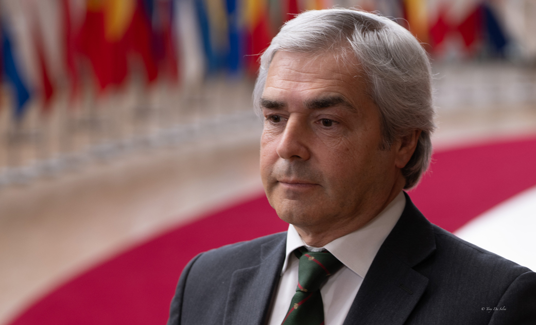 Nuno Melo, ministro da Defesa Nacional, em ambiente formal com bandeiras de vários países ao fundo, durante reunião de ministros da Defesa da União Europeia em Bruxelas.