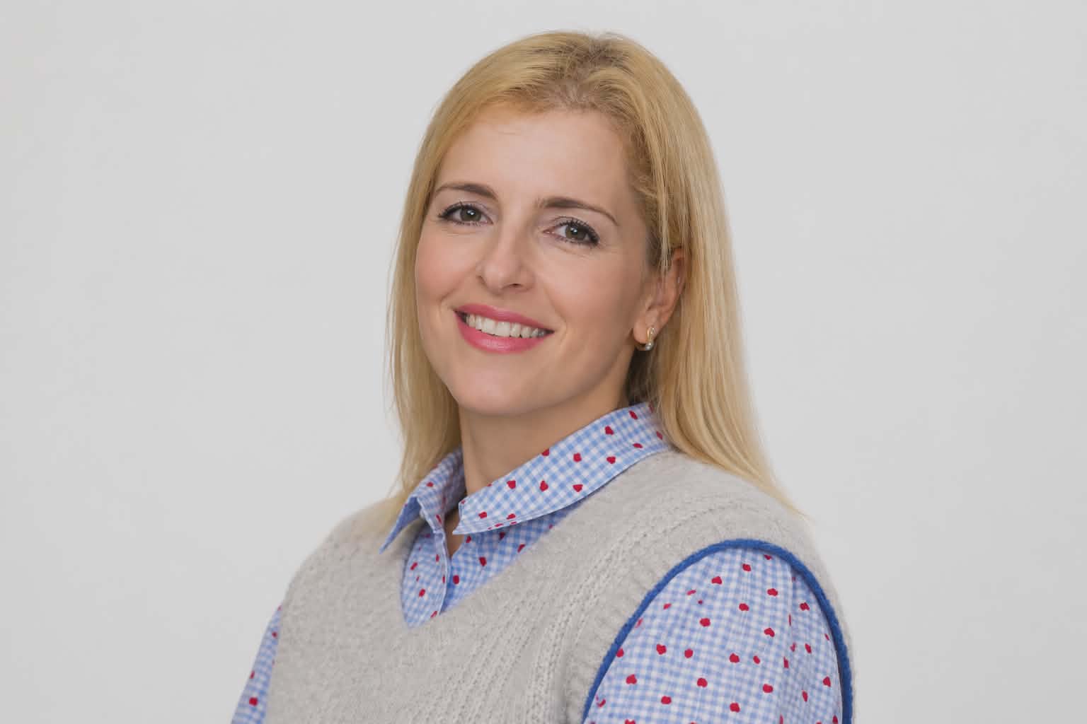 Retrato de uma pessoa adulta sorridente, com cabelo louro, vestida de forma casual, em fundo neutro, representando simbolicamente a comunidade portuguesa ativa na Bélgica.