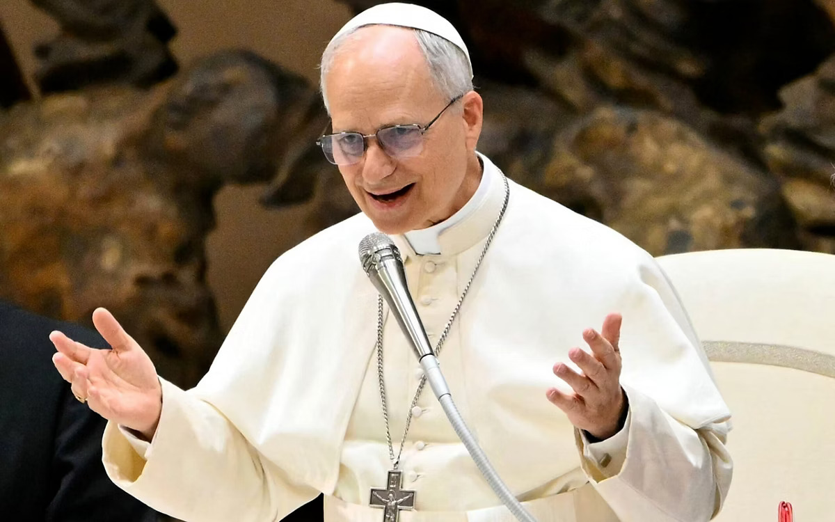Papa Leão XIV, vestido de branco, discursa num altar decorado com flores amarelas, refletindo o seu apelo à paz durante um evento académico em Roma.