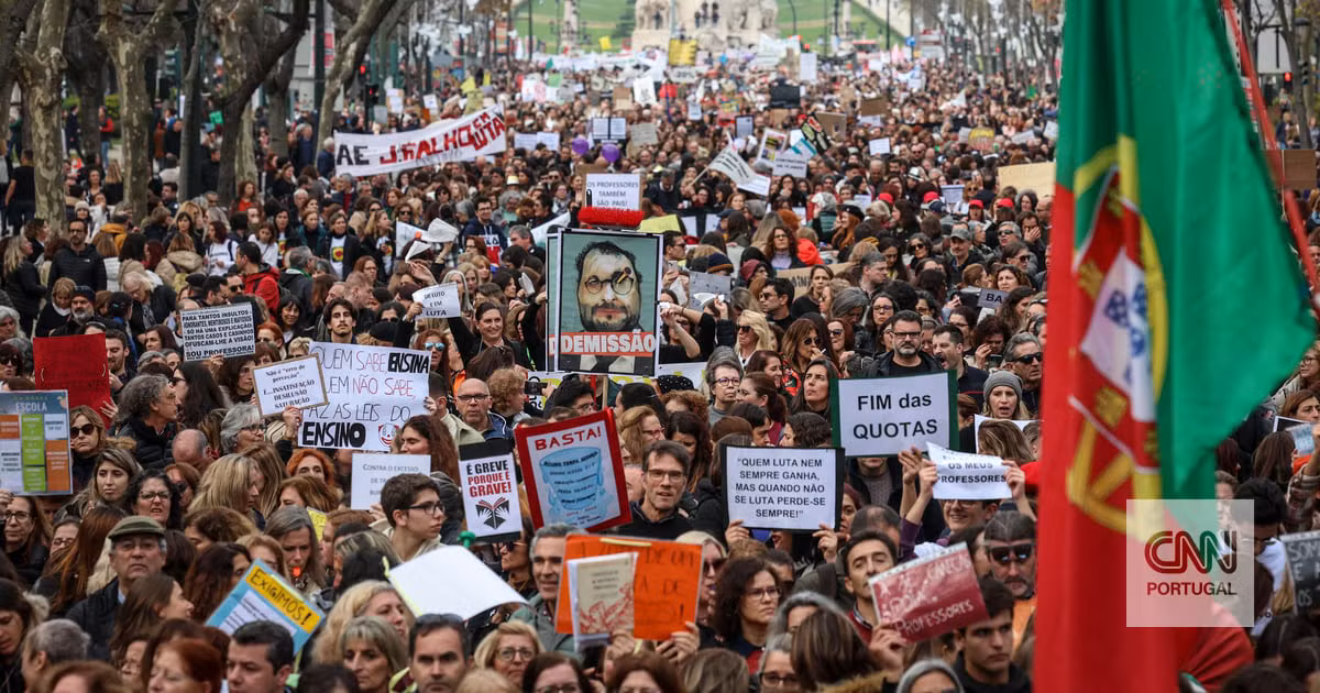 Multidão de manifestantes numa avenida, segurando cartazes de protesto e uma grande bandeira de Portugal, durante a greve geral de 11 de dezembro de 2025.