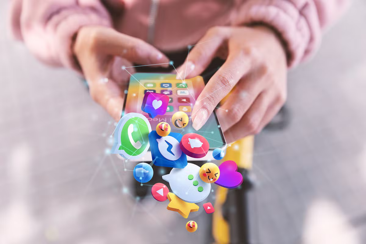 Mãos de uma pessoa a usar um smartphone, com ícones de redes sociais e emojis a sair do ecrã, simbolizando a rapidez e mistura de conteúdos nas plataformas digitais.